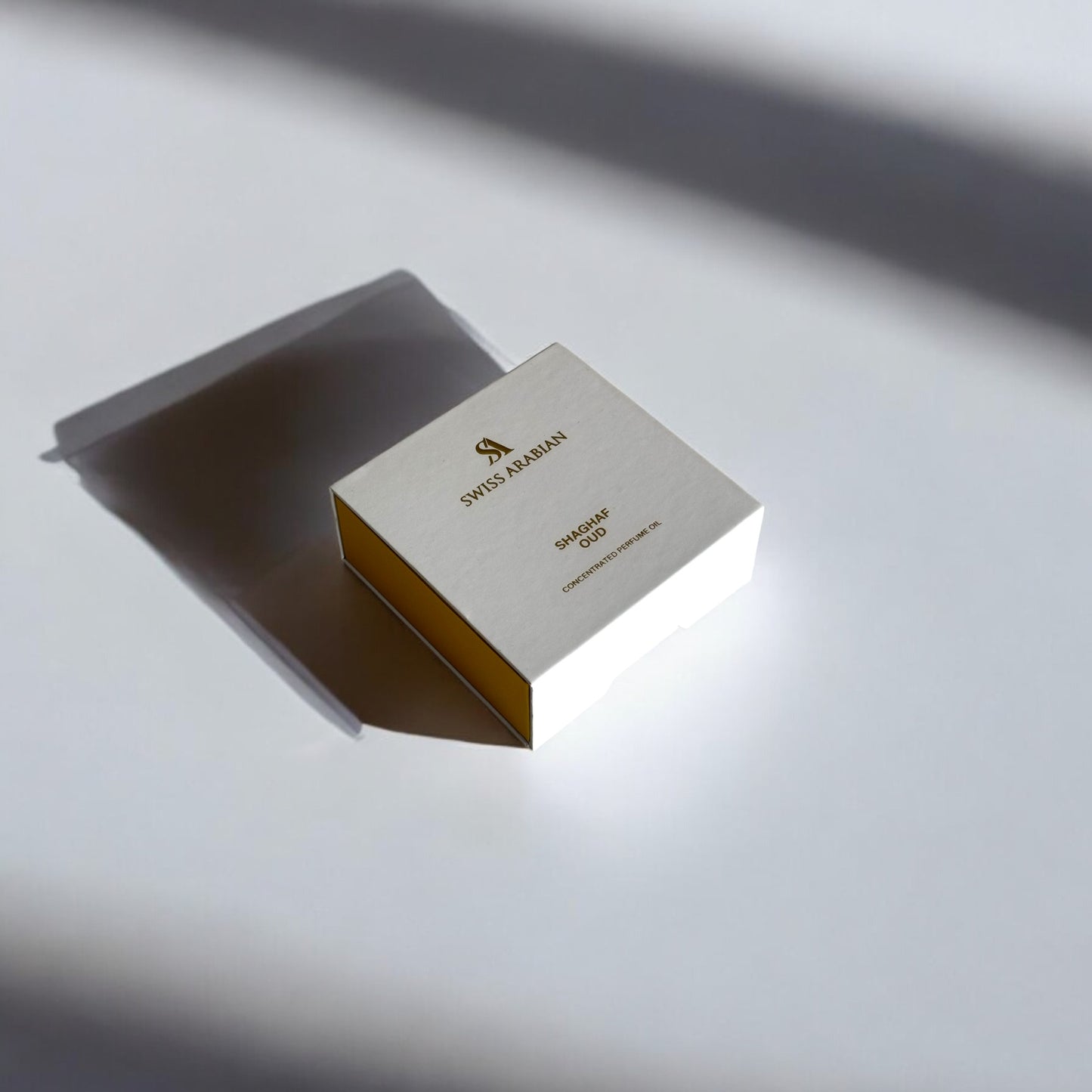 Boîte élégante de couleur crème et dorée, posée sur une surface blanche avec un jeu subtil d’ombres. L'emballage porte l'inscription 'SWISS ARABIAN' en lettres dorées, avec des détails raffinés qui évoquent une présentation luxueuse et minimaliste. L’éclairage met en valeur la texture et la finition soignée de la boîte, suggérant un produit haut de gamme
