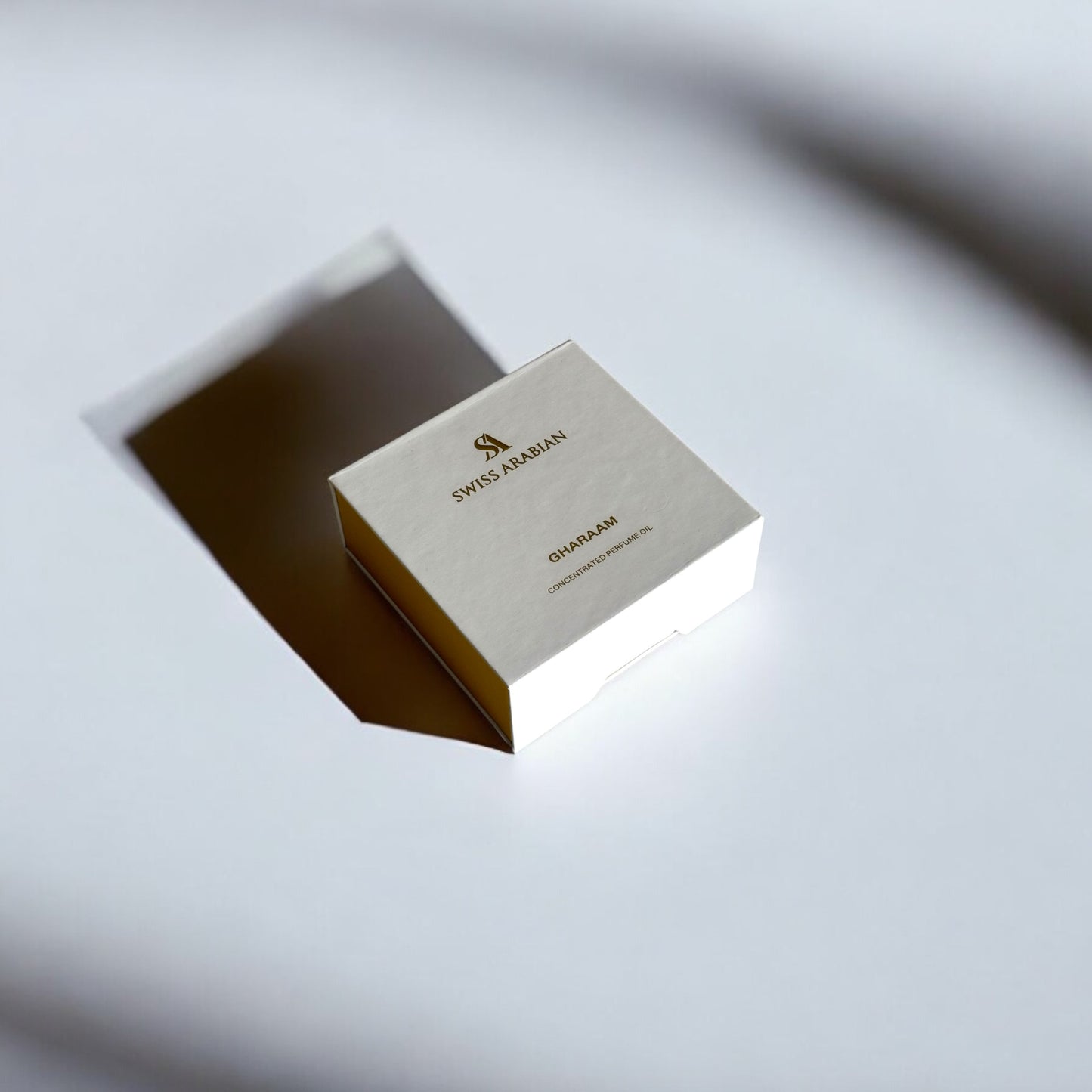 Boîte élégante de couleur crème et dorée, posée sur une surface blanche avec un jeu subtil d’ombres. L'emballage porte l'inscription 'SWISS ARABIAN' en lettres dorées, avec des détails raffinés qui évoquent une présentation luxueuse et minimaliste. L’éclairage met en valeur la texture et la finition soignée de la boîte, suggérant un produit haut de gamme