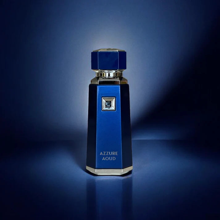 Flacon de parfum sophistiqué et luxueux, arborant une teinte bleu profond avec des finitions argentées éclatantes. Son design élancé et facetté est rehaussé par un bouchon octogonal assorti, ajoutant une touche élégante. Un ornement carré en relief avec un détail argenté est intégré au centre du flacon. L'inscription 'AZZURE AOUD' est délicatement gravée sur la face avant. Présenté sur un fond bleu avec un éclairage subtil, l’image met en valeur la brillance des finitions et l’élégance du flacon.