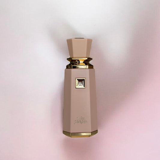 Flacon de parfum au design élégant et moderne, de couleur beige rosé avec des finitions dorées sophistiquées. Sa silhouette élancée et facettée est rehaussée par un bouchon assorti en forme de gemme. Un ornement carré en relief, agrémenté d’un détail doré, est intégré au centre du flacon, ajoutant une touche luxueuse. Présenté sur un fond doux aux nuances rose pâle et blanc, l’éclairage met en valeur la texture mate et l’éclat des accents dorés.