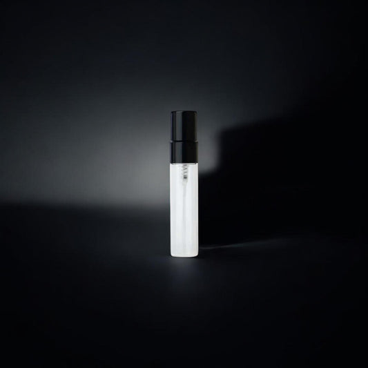 Flacon d'échantillon de parfum minimaliste et élégant, composé d'un tube en verre transparent contenant un liquide clair et d'un vaporisateur noir sobre. L’éclairage subtil met en valeur l’objet sur un fond noir avec une ombre diffuse, créant une ambiance sophistiquée et mystérieuse. L'ensemble évoque une présentation épurée et haut de gamme.